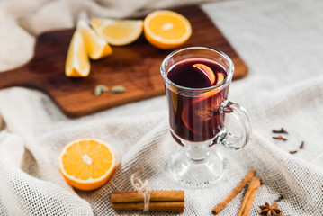 a glass of hot mulled wine on a light tablecloth, near a spice and a wooden board with orange slices.