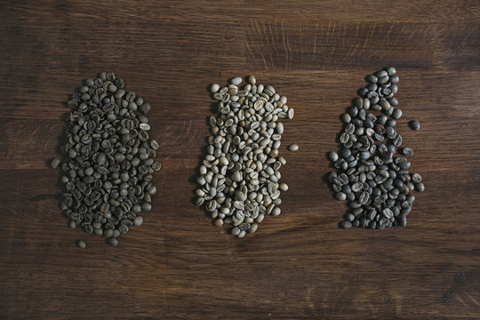 Three Piles of Unroasted Green Coffee Beans on Dark Wooden Background