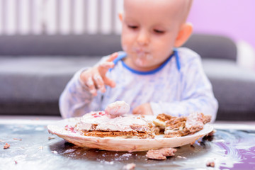 First birthday celebration of a little boy. Little boy eating birthday cake with a spoon, happy birthday. Toddler at table with cake. Little baby smash birthday cake. 