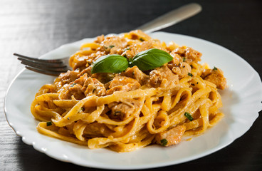 Sliced fried chicken breast meat in a creamy sauce with bavette pasta in a plate on wooden table
