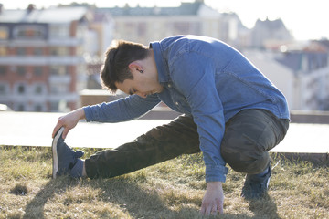 Young male parkour sportsman doing warm-up before acrobatic jumps in front of skyline