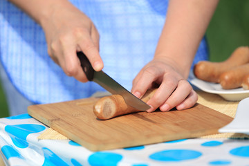 Fototapeta na wymiar Kobieta kroi nożem kiełbasę przed grilowaniem.