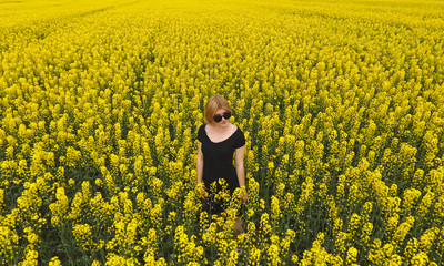 A girl in a black dress among the colors of rape in the field. W