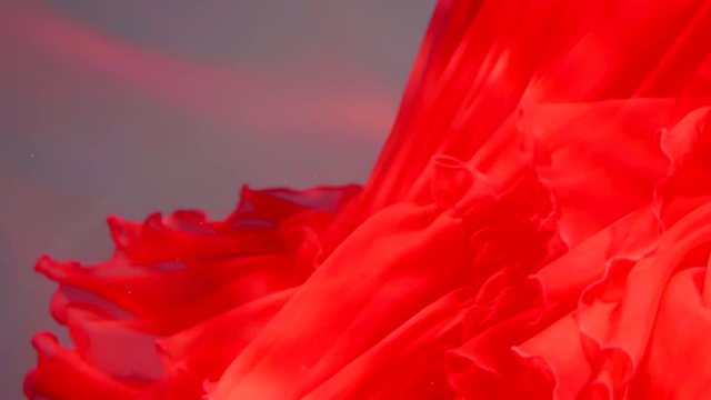 close up shot of a scarlet cloth that flutters under the water, its hem moves to the sides