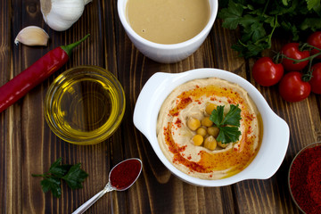 Hummus in the white plate  and ingredients on the wooden background.Top view.