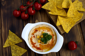 Hummus in the white plate ,cherry and chips on the wooden background.Top view.