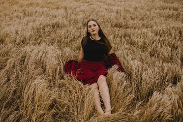 Naklejka na ściany i meble Young Woman Sitting in A Golden Wheat Field