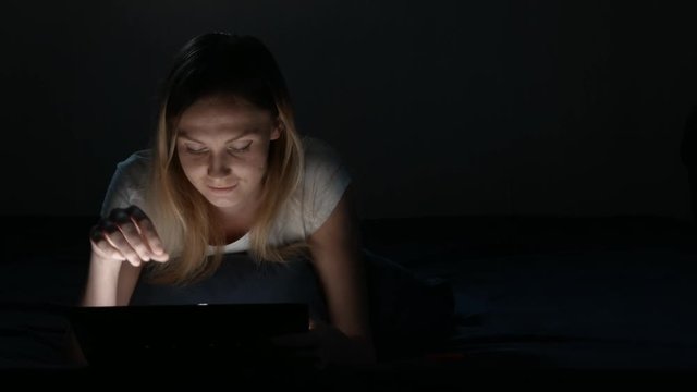 Girl uses tablet for talking in social networks. bedtime. Isolated Black. Front view. insomnia