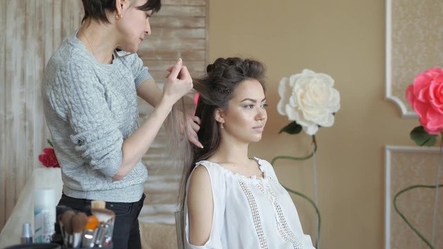 Makeup artist stylist works with model. hairdresser does the hair styling of the model. woman is working a styler with the girl's long hair. The hairdresser makes curls on the girl's straight hair