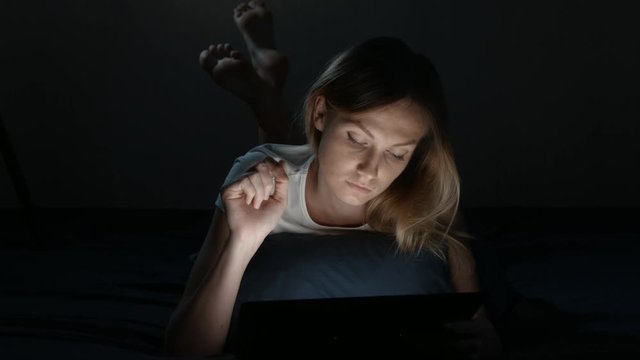 Girl is lying in a bedroom with digital tablet. Isolated Black. Front view. insomnia