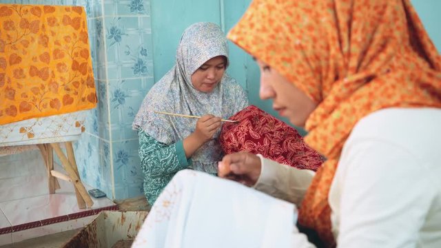Two adult indonesian women painting batik with canting