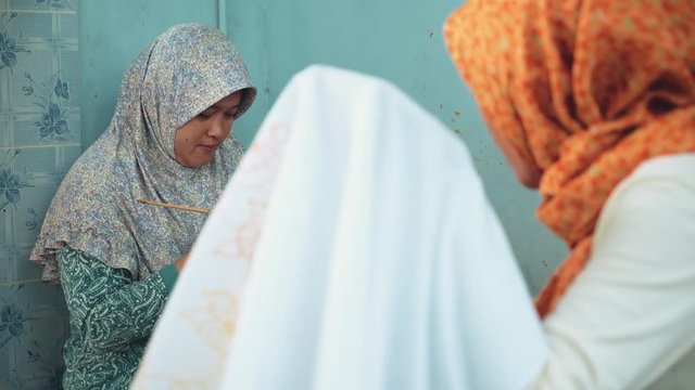 Two adult indonesian women painting batik with canting