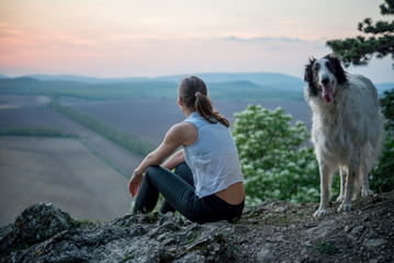 sporty girl sitting on high rock and enjoy the sunset