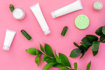 Cosmetics for skin care with natural ingredients. Eco cosmetics. Cream, lotion, oil, tonic near young green leaves on pink background top view