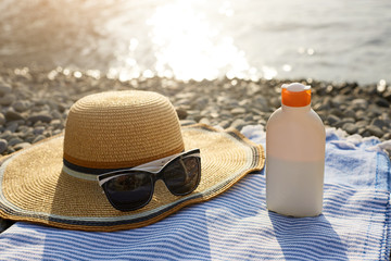 Suntan cream bottle and sunglasses on beach towel with sea shore on background. Sunscreen on deck chair outdoors on sunrise or sunset. Skin care and protection concept. Golden tan.