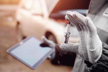 Close-up of auto mechanic holding electric candle for car. Concept diagnostics with computer.