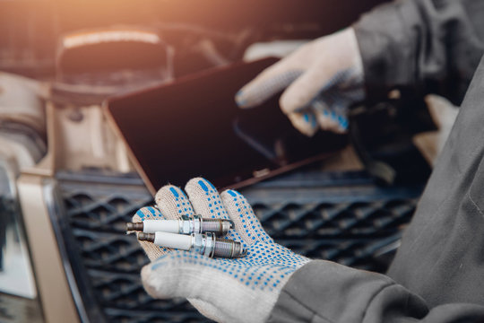 Close-up of auto mechanic holding electric candle for car. Concept diagnostics with computer.