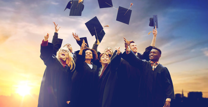 Education, Graduation And People Concept - Group Of Happy International Students In Bachelor Gowns Throwing Mortar Boards Up In The Air