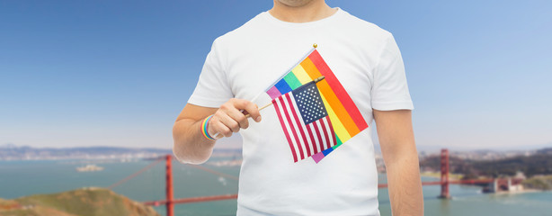 lgbt, same-sex relationships and homosexual concept - close up of man wearing gay pride rainbow awareness wristband and holding american flag over golden gate bridge in san francisco bay background