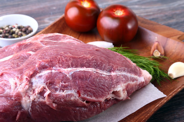 Raw pork steaks on wooden board with herbs, garlic, spices and tomatoes ready for cooking. Selective focus.