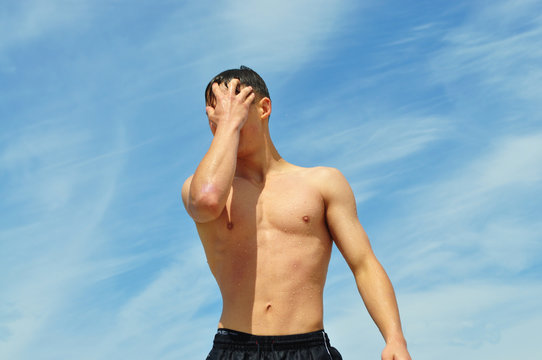 a handsome guy with a relief figure, with a naked torso against the sea and sky, corrects the hair covering his face with his hand