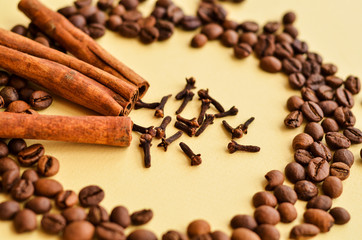 three sticks of cinnamon in a circle of coffee beans and clove spice on a yellow background