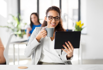 business, technology and people concept - african american businesswoman with tablet pc computer drinking coffee at office