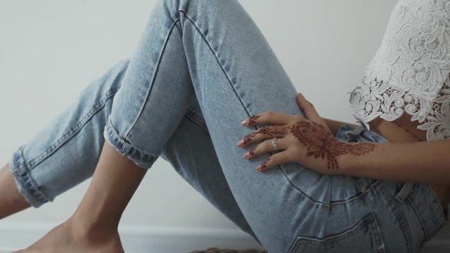 Lovely woman sitting on a parquet alone in house. Henna on hands. Scandinavian interior. Jeans and blouse.