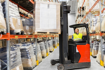 wholesale, logistic, shipment and people concept - loader operating forklift and loading boxes at warehouse