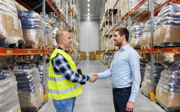 logistic business and cooperation concept - manual worker and businessman with clipboard shaking hands and making deal at warehouse