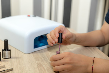 Woman applying color polish to fingernails with brush. Nail drying machine.