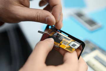 Close up of repairman's hands holding parts of disassembled damaged faulty smart phone using special tools and equipment at his workplace. Modern electronic maintenance and repair service concept