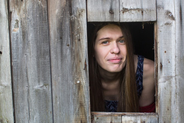 Young woman with long hair looks out of the wooden shed windows.