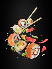 Différents rouleaux de sushi frais avec des baguettes congelées dans l& 39 air sur fond noir