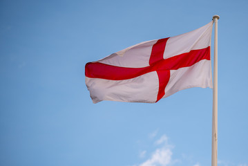 national flag of England St Georges flag blowing in the wind with blue sky in background