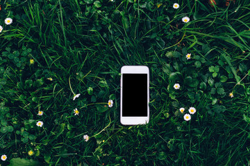 Close-up of a phone with a screen off which lies in the green grass