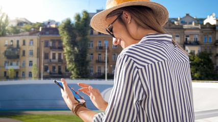 Fototapeta premium Portrait of beautiful stylish woman in hat using mobile phone on street at sunny summer day