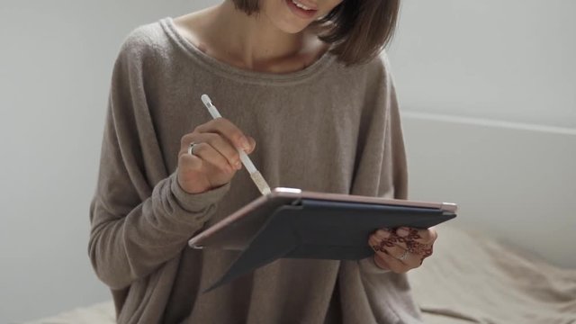 close up shot of the lady who holds a portable tablet in her hand, the lady drives a pencil around the gadget and is doing online business in her apartment