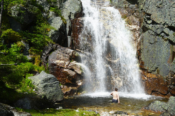 Man walking into the waterfall alone. Travel Lifestyle adventure concept of an active vacations into the wild nature.