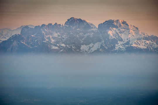 Sunrise on snow-covered Mount Schiara peaks dipped in the mist, Dolomites, Veneto, Italy