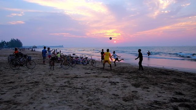CHAUNG THA, MYANMAR - FEBRUARY 28, 2018: The group of teenagers play chinlone (cane ball) game next to bicycle rental point on the sunset beach of resort, on February 28 in Chaung Tha.