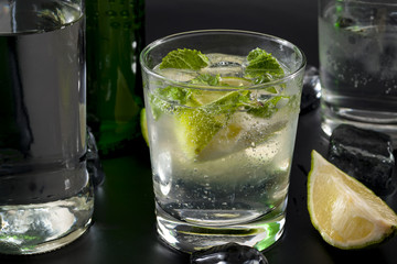 Refreshing cocktails and mixed alcoholic drinks concept with close up of a glass of gin and tonic on a bar counter with a bottle of gin, mineral water, mint leaves and slices of lime