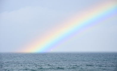 Rainbow over the sea. Seascape with beautiful multicoloured rainbow over the sea. White sailing boat in the background.
