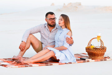 lovely attractive couple sitting together on the white sand beach, happy couple sitting on a blanket , happy couple enjoying picnic on the beach and have good time on summer vacations