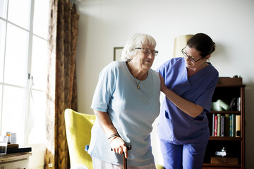 Nurse helping senior woman to stand - obrazy, fototapety, plakaty
