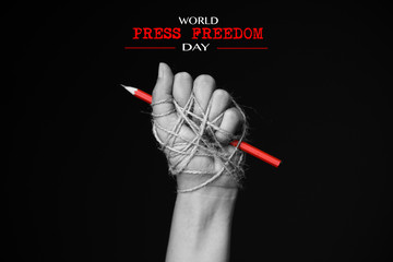 Hand with red pencil tied with rope, depicting the idea of freedom of the press or freedom of...