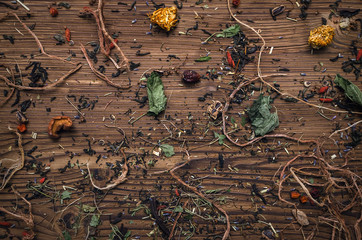 Herbal medicine concept background with scattered herbs and dry flower leaves on brown wooden table.