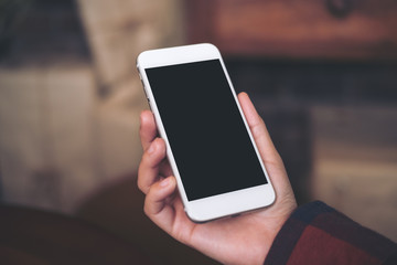 Mockup image of hand holding white mobile phone with blank black screen in cafe