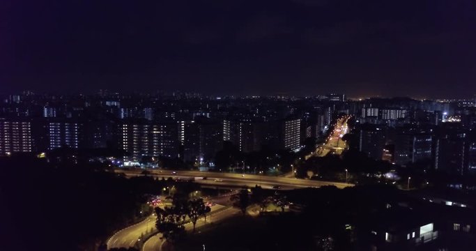 Aerial view of high way and apartment buildings lit up at night from Jurong West in Singapore. Aerial drone shot, yellow and blue tones