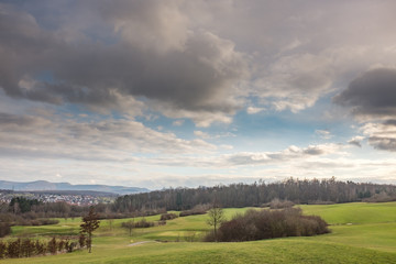 Fototapeta na wymiar Hügelige Landschaft mit Wolkenspiel und vereinzelten Schneeflocken